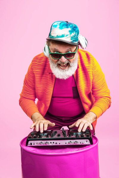 Senior hipster man wearing eyeglasses posing on pink background. Tech and joyful elderly lifestyle concept