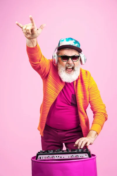 Senior hipster man bär glasögon poserar på rosa bakgrund. Tekniskt och glädjefyllt äldre livsstil koncept — Stockfoto
