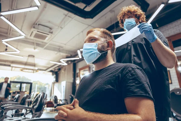 Homem cortando o cabelo na barbearia usando máscara durante a pandemia de coronavírus — Fotografia de Stock