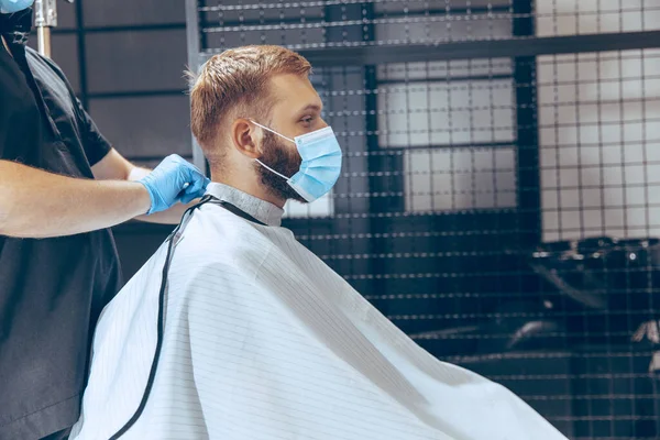 Hombre que se corta el pelo en la barbería usando máscara durante la pandemia de coronavirus — Foto de Stock