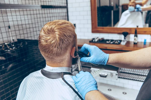 Hombre que se corta el pelo en la barbería usando máscara durante la pandemia de coronavirus — Foto de Stock