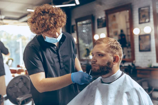 Man getting hair cut at the barbershop wearing mask during coronavirus pandemic