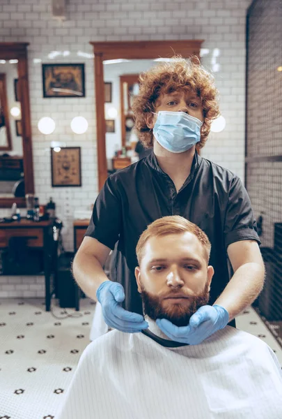 Homem cortando o cabelo na barbearia usando máscara durante a pandemia de coronavírus — Fotografia de Stock