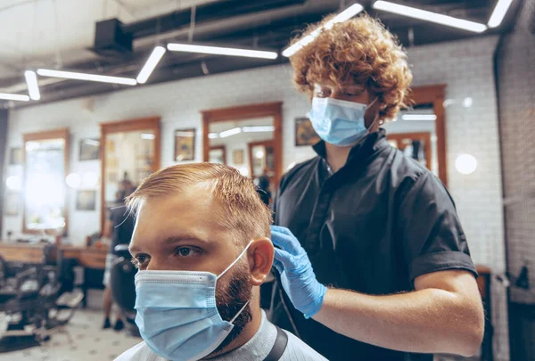 Hombre que se corta el pelo en la barbería usando máscara durante la pandemia de coronavirus — Foto de Stock