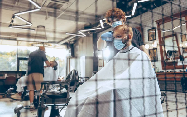 Man getting hair cut at the barbershop wearing mask during coronavirus pandemic