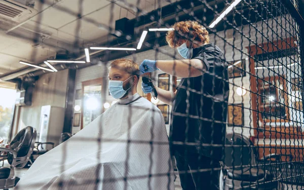 Man getting hair cut at the barbershop wearing mask during coronavirus pandemic