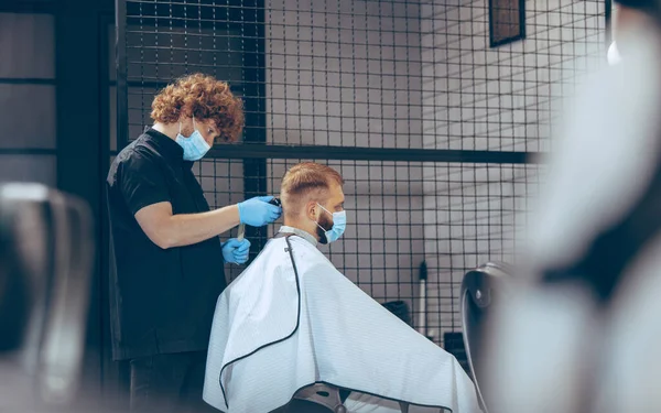 Man getting hair cut at the barbershop wearing mask during coronavirus pandemic