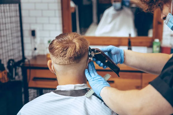 Man getting hair cut at the barbershop wearing mask during coronavirus pandemic