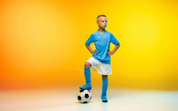 Niño joven como futbolista o futbolista en ropa deportiva practicando en degradado fondo de estudio amarillo en luz de neón — Foto de Stock