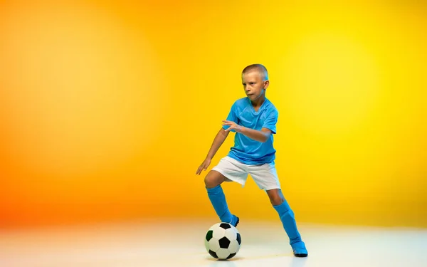 Genç bir çocuk spor giyiminde futbol oyuncusu ya da neon ışıklı arka planda gradyan sarı stüdyoda antrenman yapıyor. — Stok fotoğraf