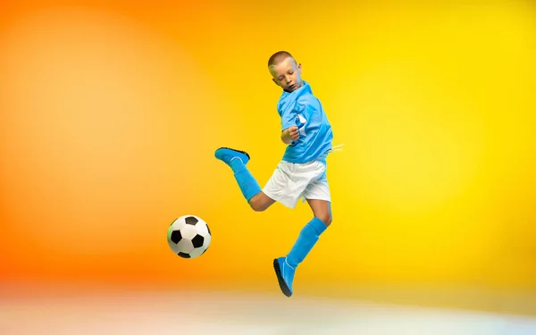 Menino como um jogador de futebol ou futebol em sportwear praticando em gradiente amarelo estúdio fundo em luz de néon — Fotografia de Stock