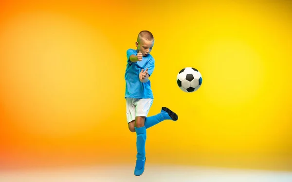 Menino como um jogador de futebol ou futebol em sportwear praticando em gradiente amarelo estúdio fundo em luz de néon — Fotografia de Stock