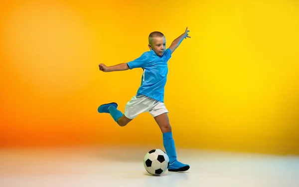 小男孩作为足球或足球运动员，穿着运动鞋，在渐变黄色工作室的背景下，在霓虹灯下练习 — 图库照片