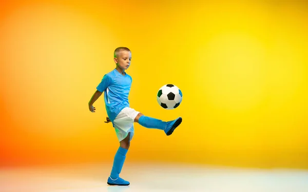 Menino como um jogador de futebol ou futebol em sportwear praticando em gradiente amarelo estúdio fundo em luz de néon — Fotografia de Stock