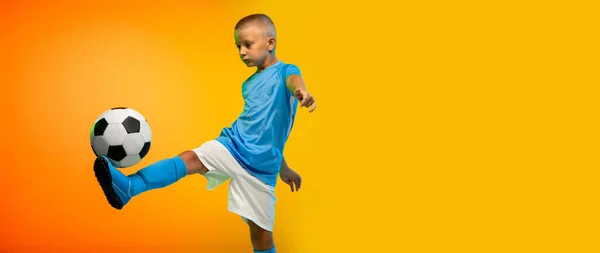 Menino como um jogador de futebol ou futebol em sportwear praticando em gradiente amarelo estúdio fundo em luz de néon — Fotografia de Stock