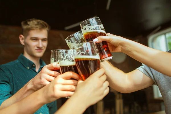 Giovani amici che bevono birra, si divertono, ridono e festeggiano insieme. Chiudere clinking bicchieri di birra — Foto Stock