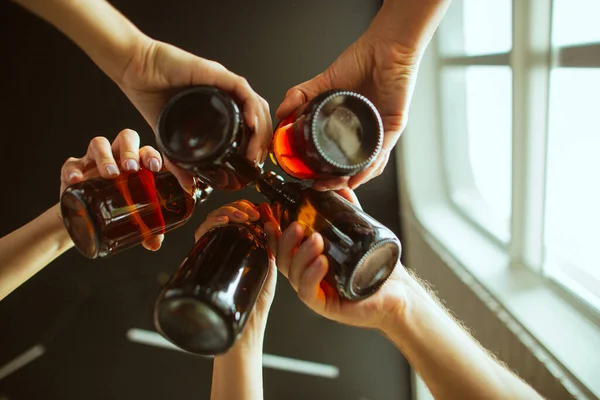 Giovani amici che bevono birra, si divertono, ridono e festeggiano insieme. Chiudere clinking bottiglie di birra — Foto Stock