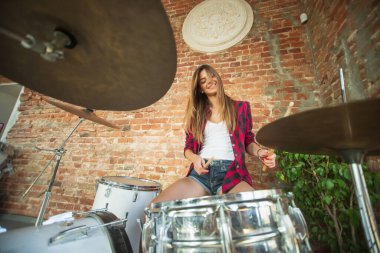 Kadın iş yerinde ya da evde otururken müzik kaydediyor, şarkı söylüyor ve davul çalıyor.