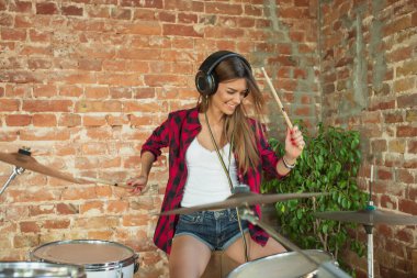 Kadın iş yerinde ya da evde otururken müzik kaydediyor, şarkı söylüyor ve davul çalıyor.