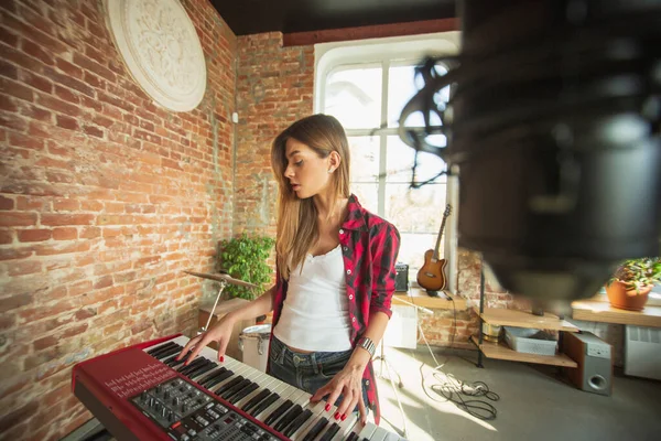 Vrouw die muziek opneemt, zingt en piano speelt terwijl ze op zolder of thuis staat — Stockfoto