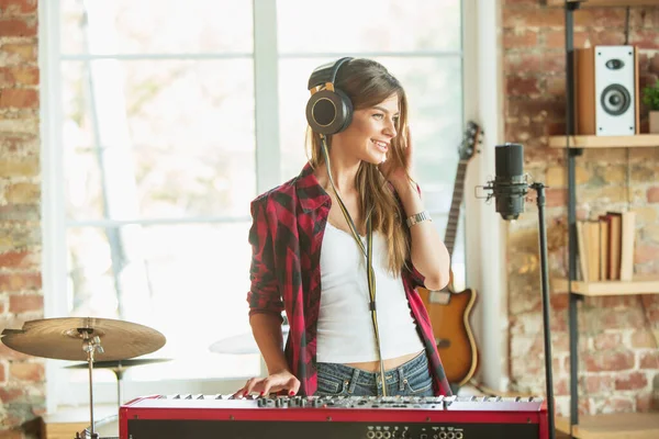 Woman recording music, singing and playing piano while standing in loft workplace or at home