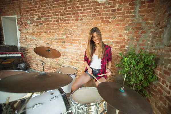 Woman recording music, singing and playing drums while sitting in loft workplace or at home