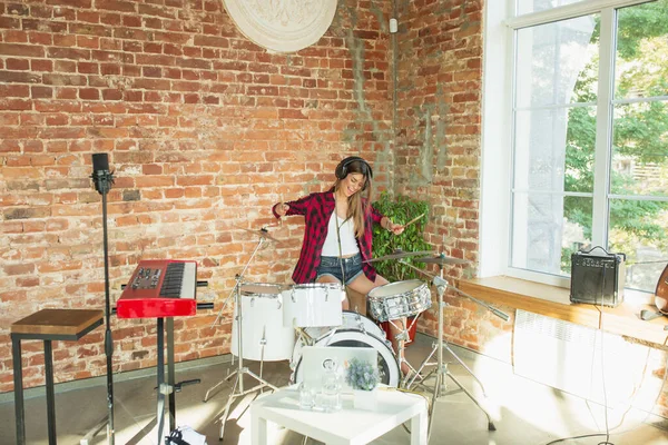 Woman recording music, singing and playing drums while sitting in loft workplace or at home