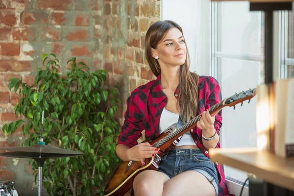 Çatı katında ya da evde otururken müzik kaydeden, şarkı söyleyen ve gitar çalan bir kadın