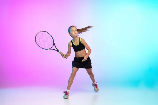 Little tennis girl in black sportwear isolated on gradient background in neon light — Stock Photo, Image