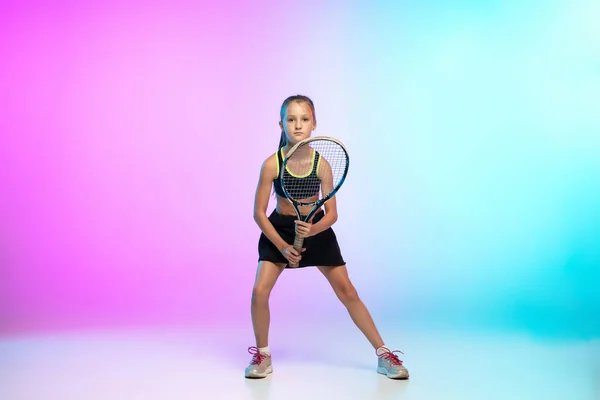 Little tennis girl in black sportwear isolated on gradient background in neon light — Stock Photo, Image