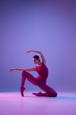 Genç ve zarif balerin mor stüdyo arka planında neon ışıkta izole edilmiş.