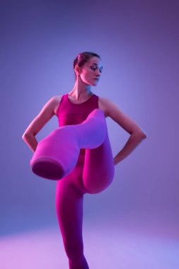 Genç ve zarif balerin mor stüdyo arka planında neon ışıkta izole edilmiş.