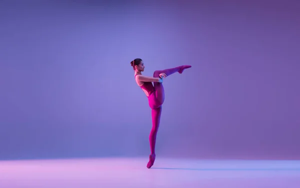 Jovem e graciosa bailarina de balé isolado em fundo estúdio roxo em luz de néon — Fotografia de Stock