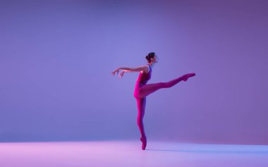 Genç ve zarif balerin mor stüdyo arka planında neon ışıkta izole edilmiş.