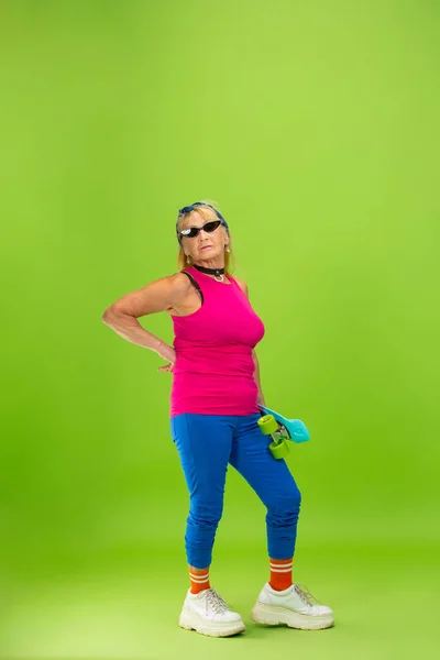 Старшая женщина в ультра модной одежде изолированы на ярко-зеленом фоне — стоковое фото