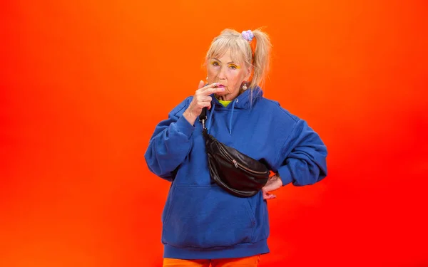 Donna anziana in abbigliamento ultra trendy isolato su sfondo arancione brillante — Foto Stock