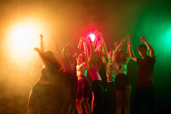 Una folla di persone in silhouette alza le mani sulla pista da ballo su sfondo luce al neon — Foto Stock