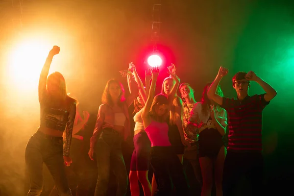 Una multitud de personas en silueta levanta sus manos en la pista de baile sobre fondo de luz de neón —  Fotos de Stock