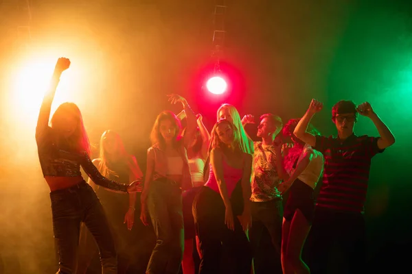 A crowd of people in silhouette raises their hands on dancefloor on neon light background — Stock Photo, Image