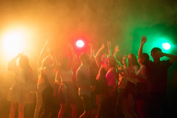 A crowd of people in silhouette raises their hands on dancefloor on neon light background — Stock Photo, Image