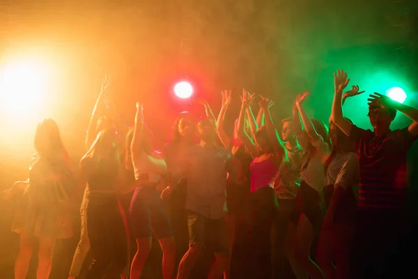 Una multitud de personas en silueta levanta sus manos en la pista de baile sobre fondo de luz de neón —  Fotos de Stock