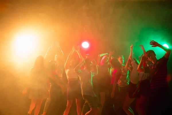 Uma multidão de pessoas em silhueta levanta as mãos na pista de dança no fundo de luz de néon — Fotografia de Stock