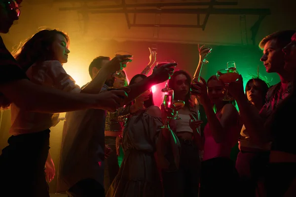 Una multitud de personas en silueta levanta sus manos en la pista de baile sobre fondo de luz de neón —  Fotos de Stock