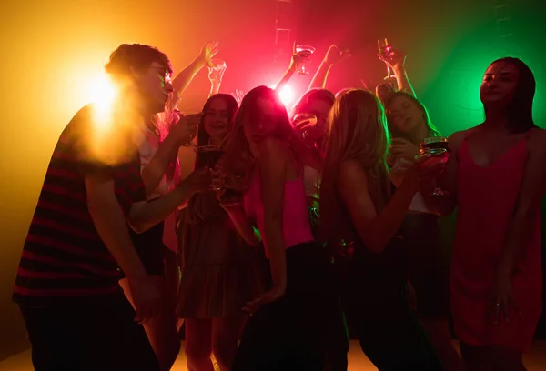 A crowd of people in silhouette raises their hands on dancefloor on neon light background — Stock Photo, Image