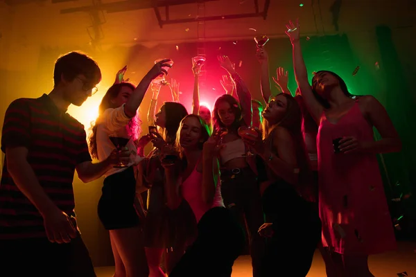 A crowd of people in silhouette raises their hands on dancefloor on neon light background — Stock Photo, Image