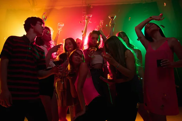 A crowd of people in silhouette raises their hands on dancefloor on neon light background — Stock Photo, Image