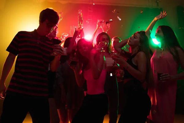 Una multitud de personas en silueta levanta sus manos en la pista de baile sobre fondo de luz de neón — Foto de Stock