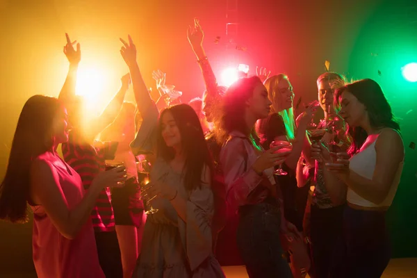 A crowd of people in silhouette raises their hands on dancefloor on neon light background — Stock Photo, Image