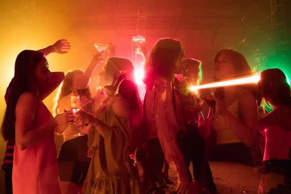 A crowd of people in silhouette raises their hands on dancefloor on neon light background — Stock Photo, Image