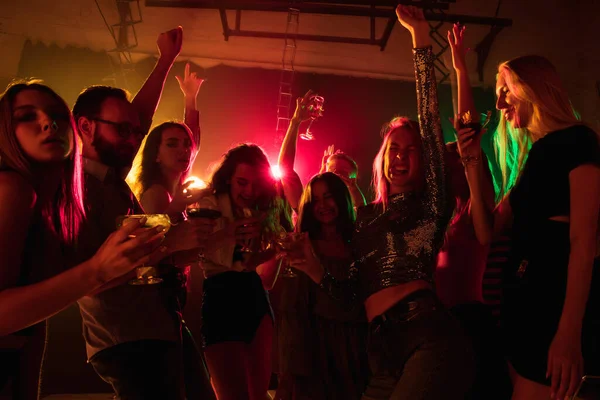 A crowd of people in silhouette raises their hands on dancefloor on neon light background — Stock Photo, Image